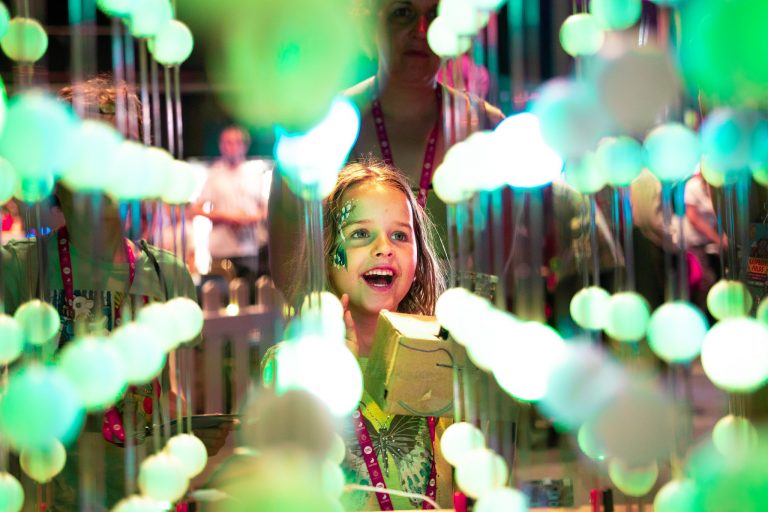 Child looking up through colourful hanging lights
