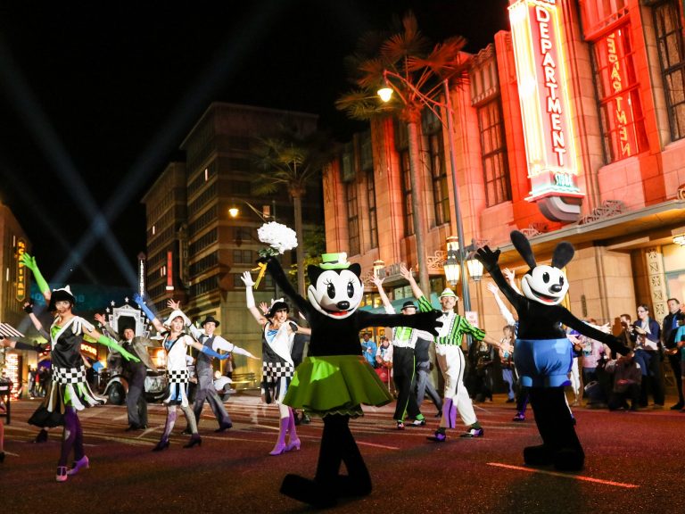 Night-time parade passing illuminated city buildings