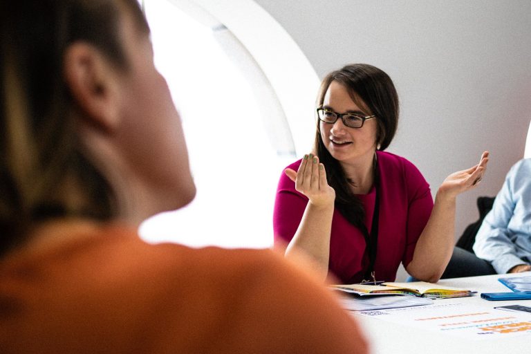 Woman in a magenta top speaking across a meeting table