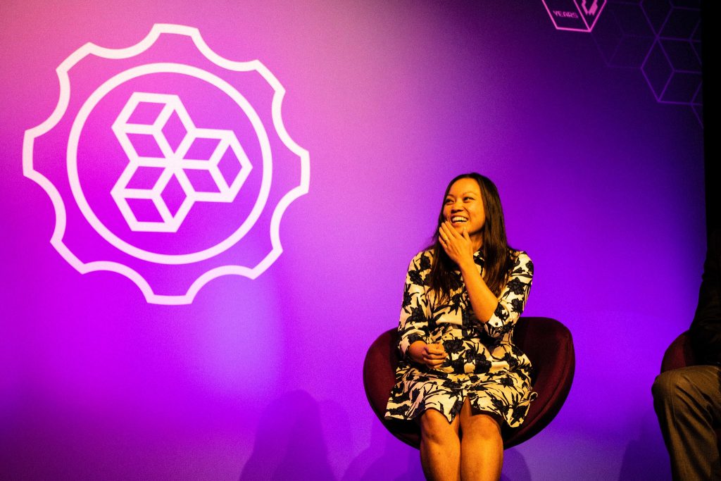 Woman speaking during a panel under purple stage lighting