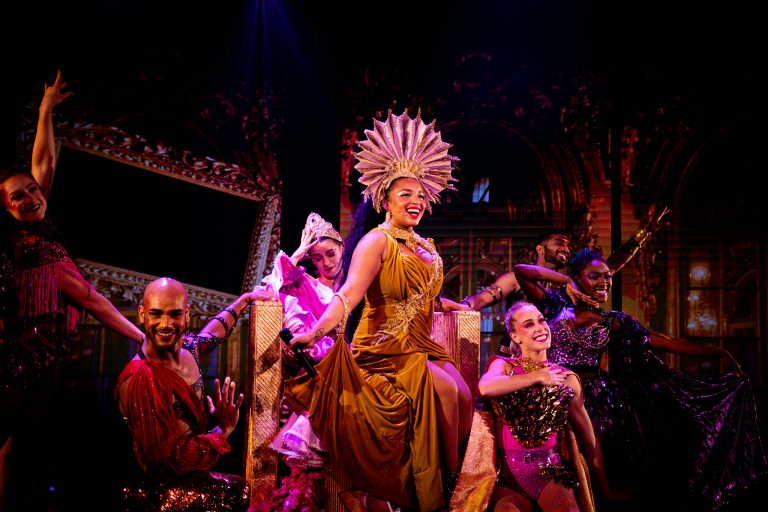Theatre ensemble in gold costumes under warm stage lighting