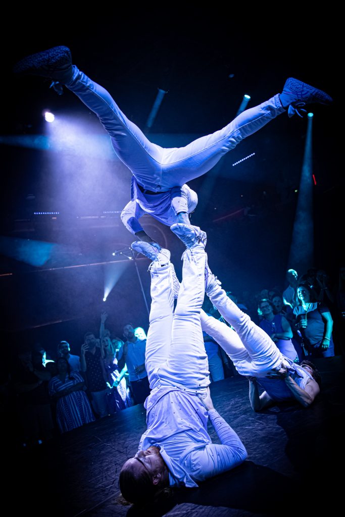 Acrobats supporting an upside-down performer under blue light