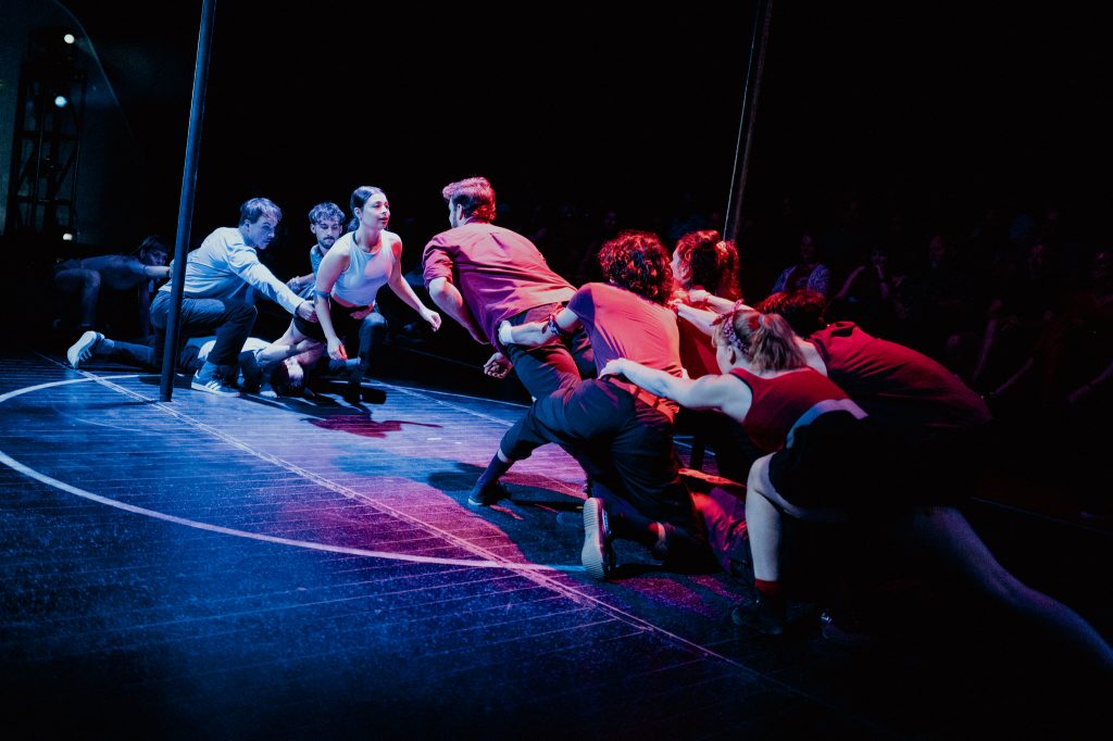 Dance ensemble reaching across a red and blue stage