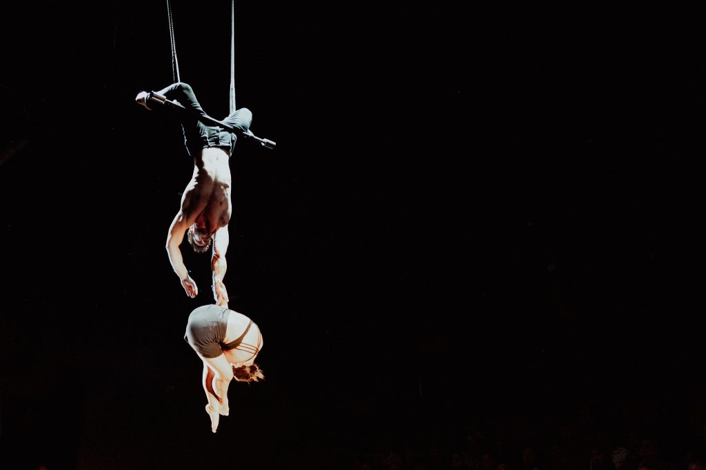 Two aerial acrobats suspended against a black stage