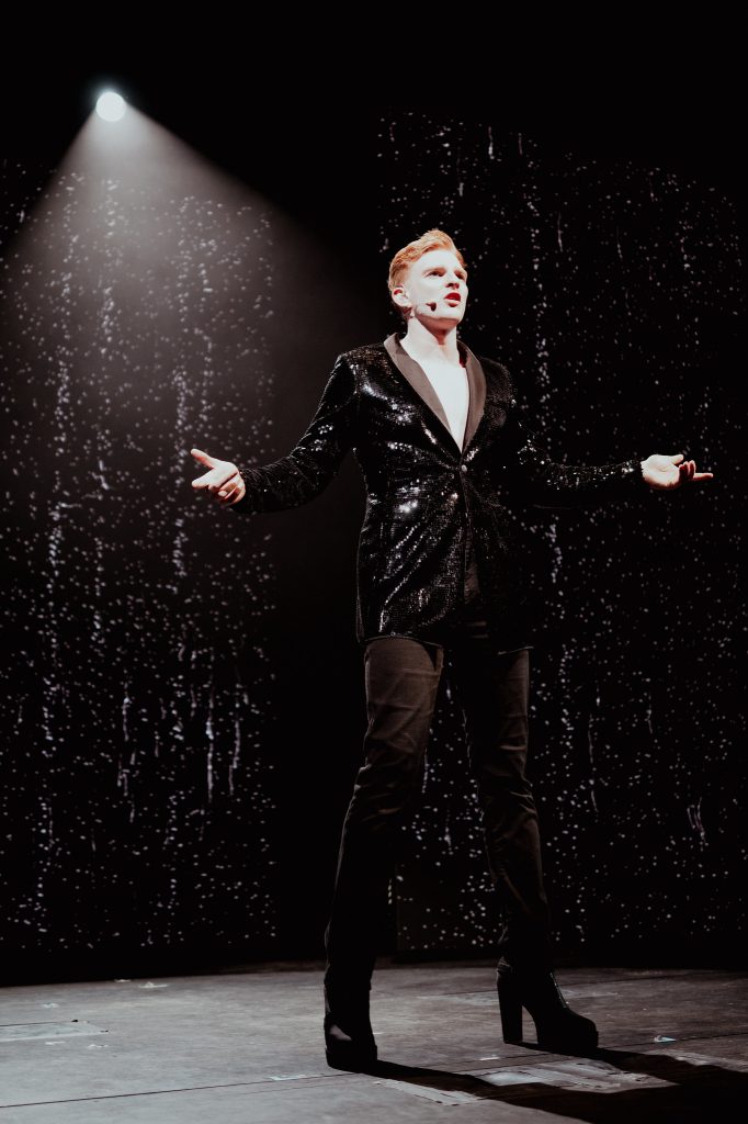 Male singer performing alone under a white spotlight