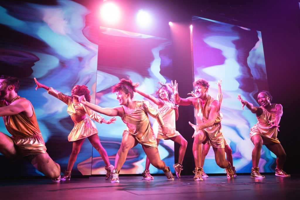 Dance ensemble performing beneath pink and blue lights
