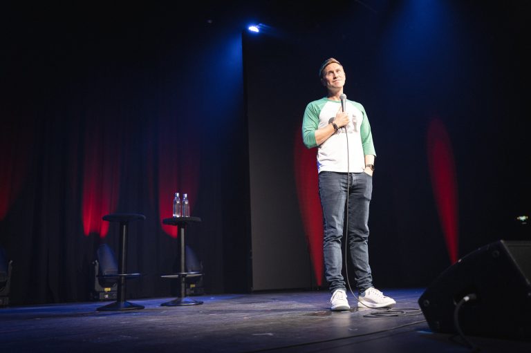 Male performer speaking into a microphone under a spotlight