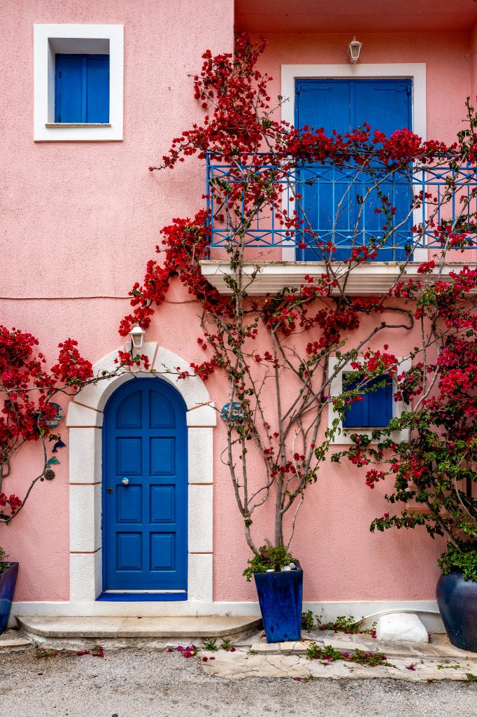 Blue door and balcony on a pink wall covered in red leaves