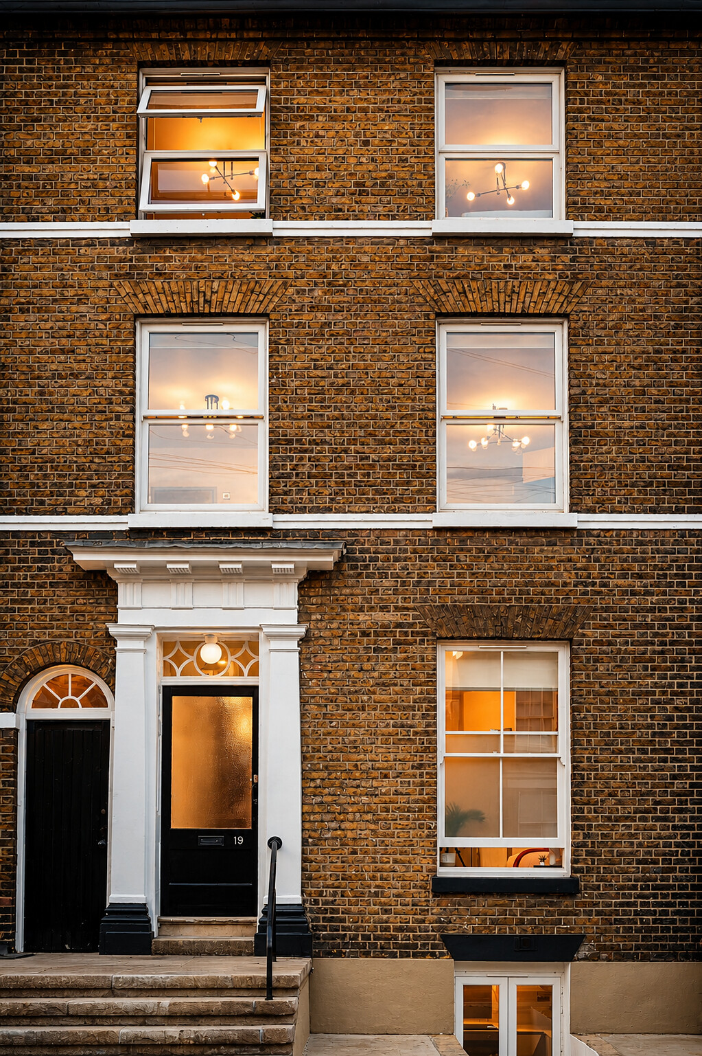 Tall brick frontage with illuminated windows and a black entrance door